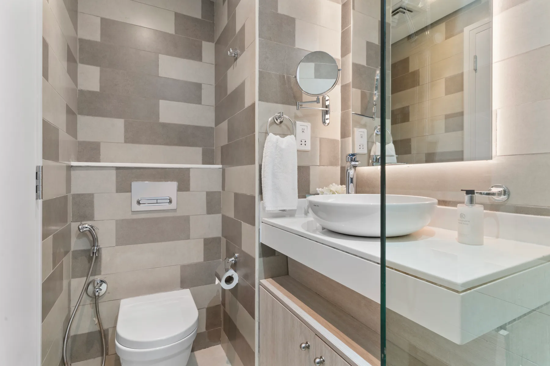 Un baño moderno con inodoro, lavabo suspendido y paredes revestidas de azulejos.