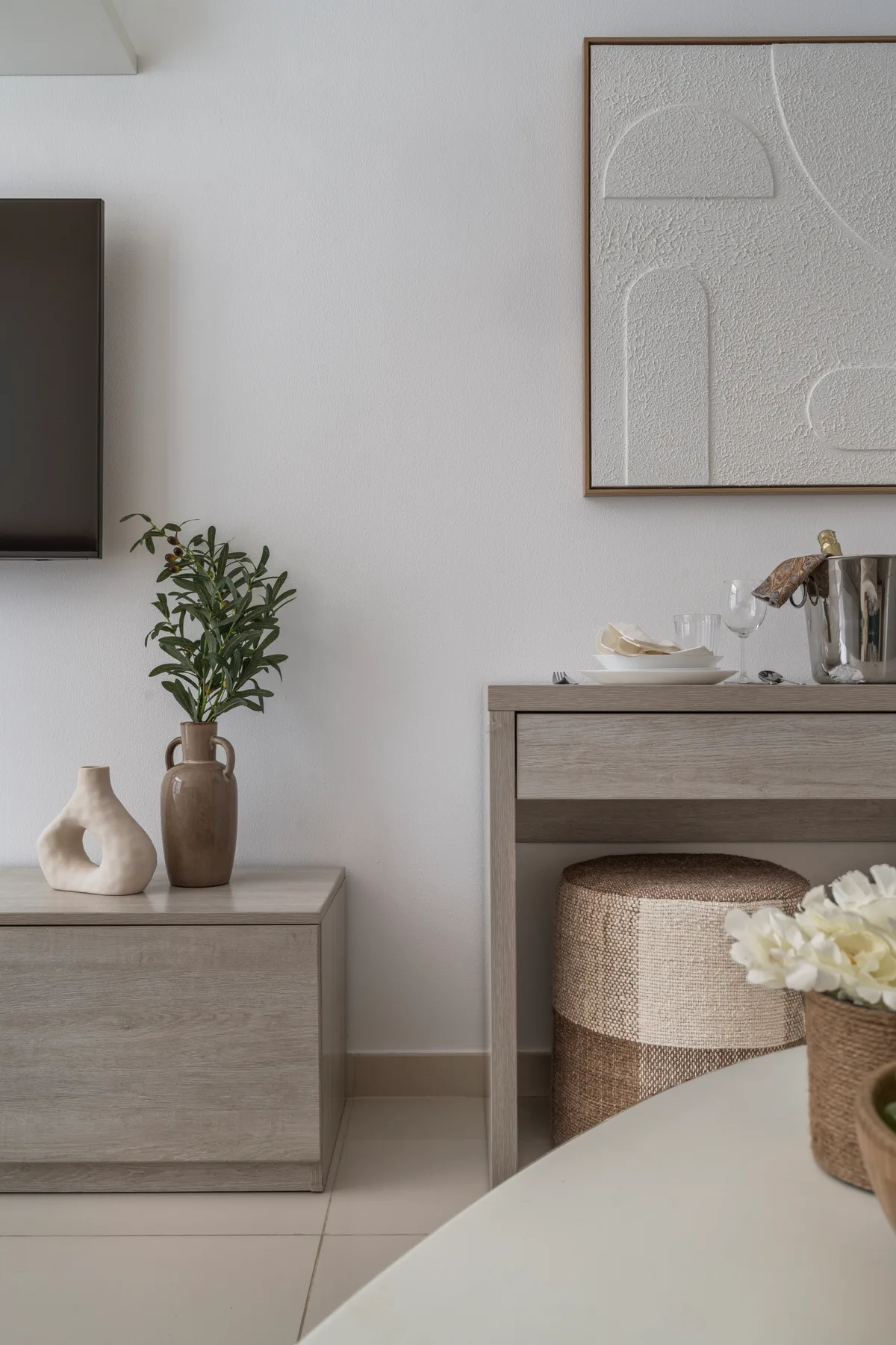 Un rincón tranquilo de dormitorio con muebles de madera clara, arte enmarcado y una planta pequeña.