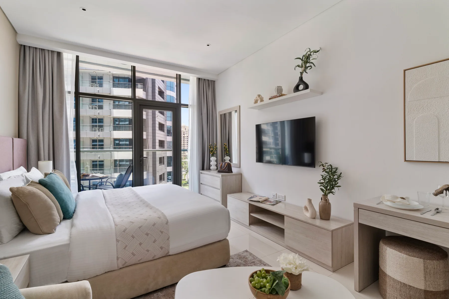 Dormitorio con una cama junto a grandes ventanales y un televisor.
