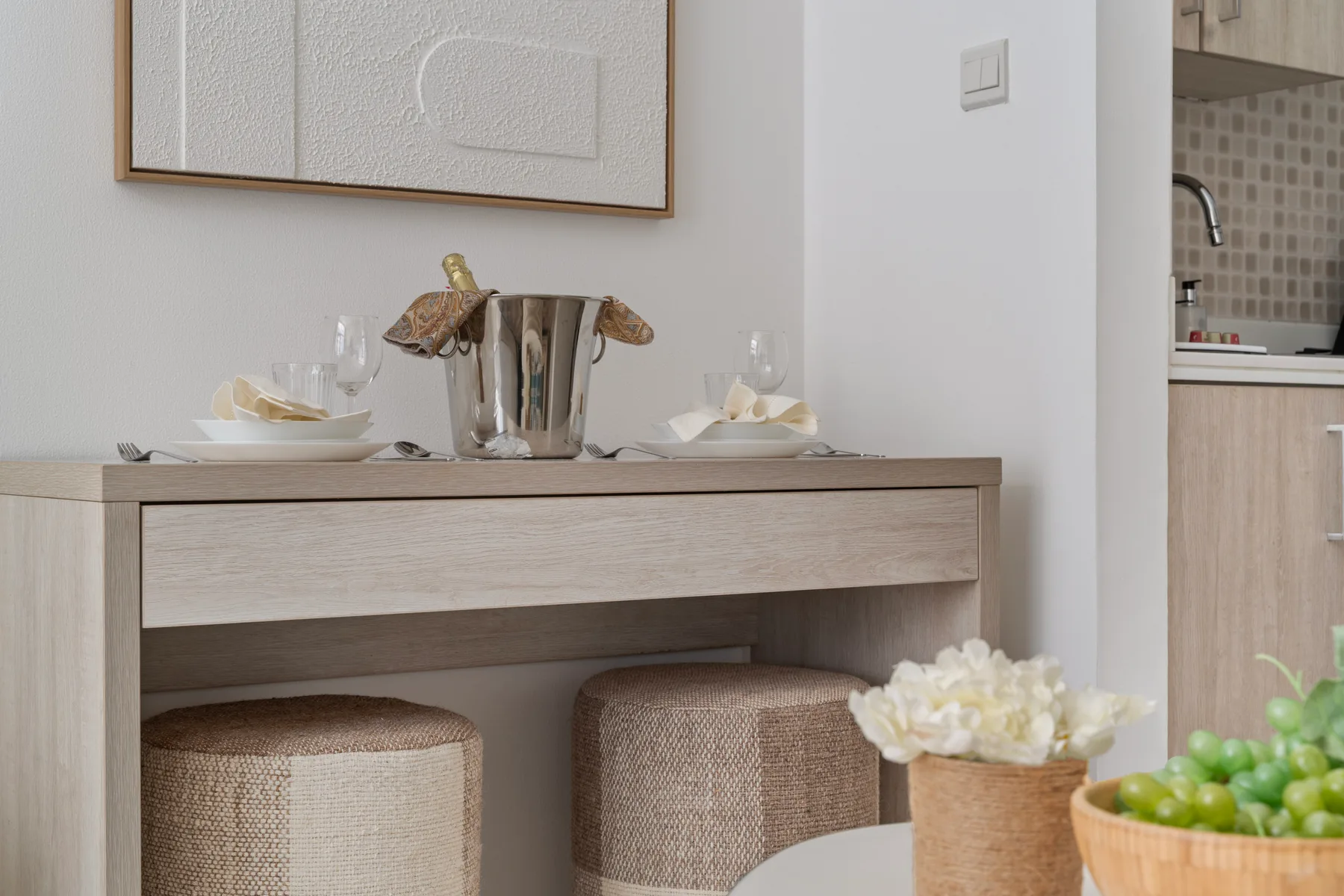 Comedor con la mesa puesta y asientos tapizados bajo un cuadro enmarcado.
