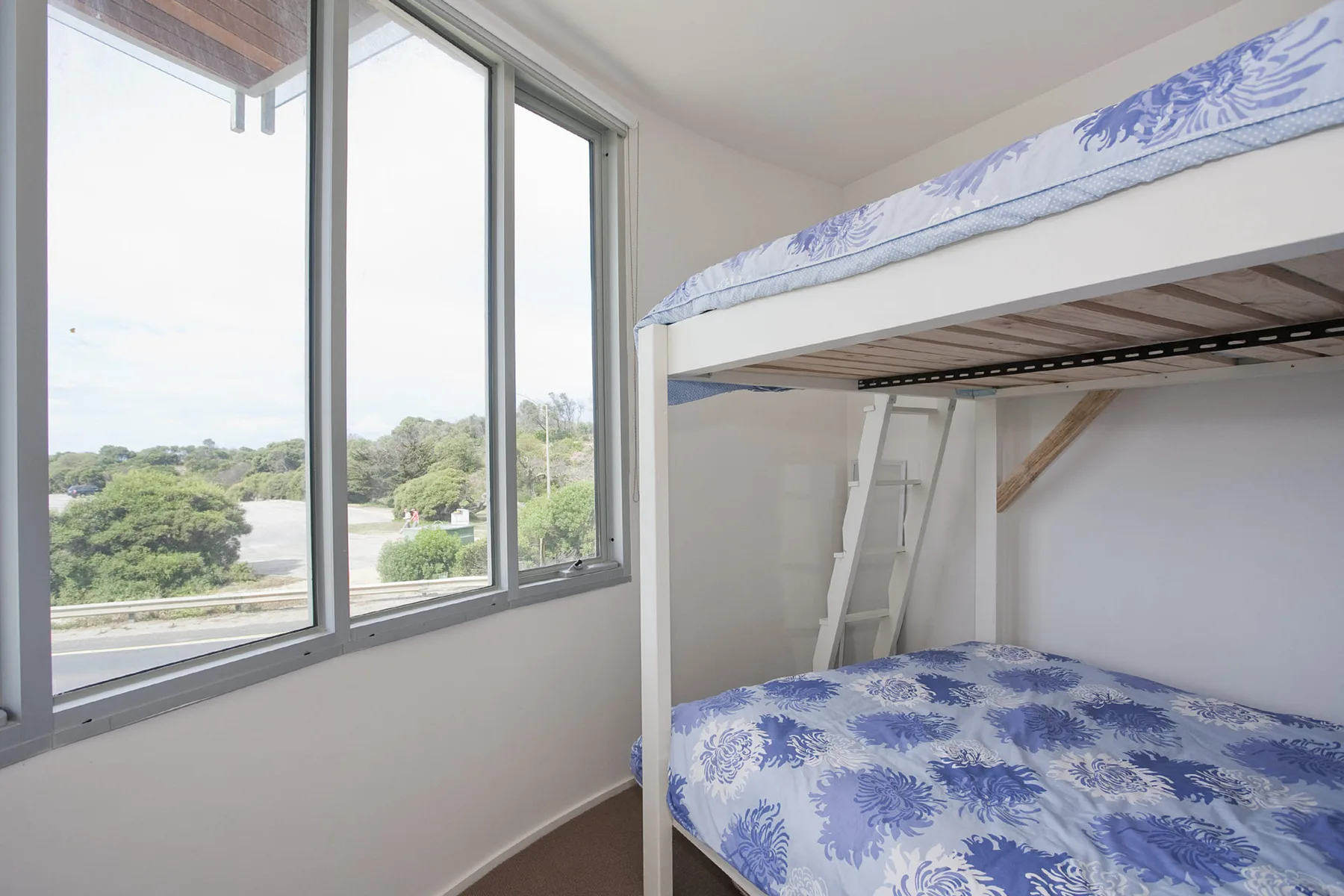 Un dormitorio con una litera junto a grandes ventanas con vista a la vegetación.