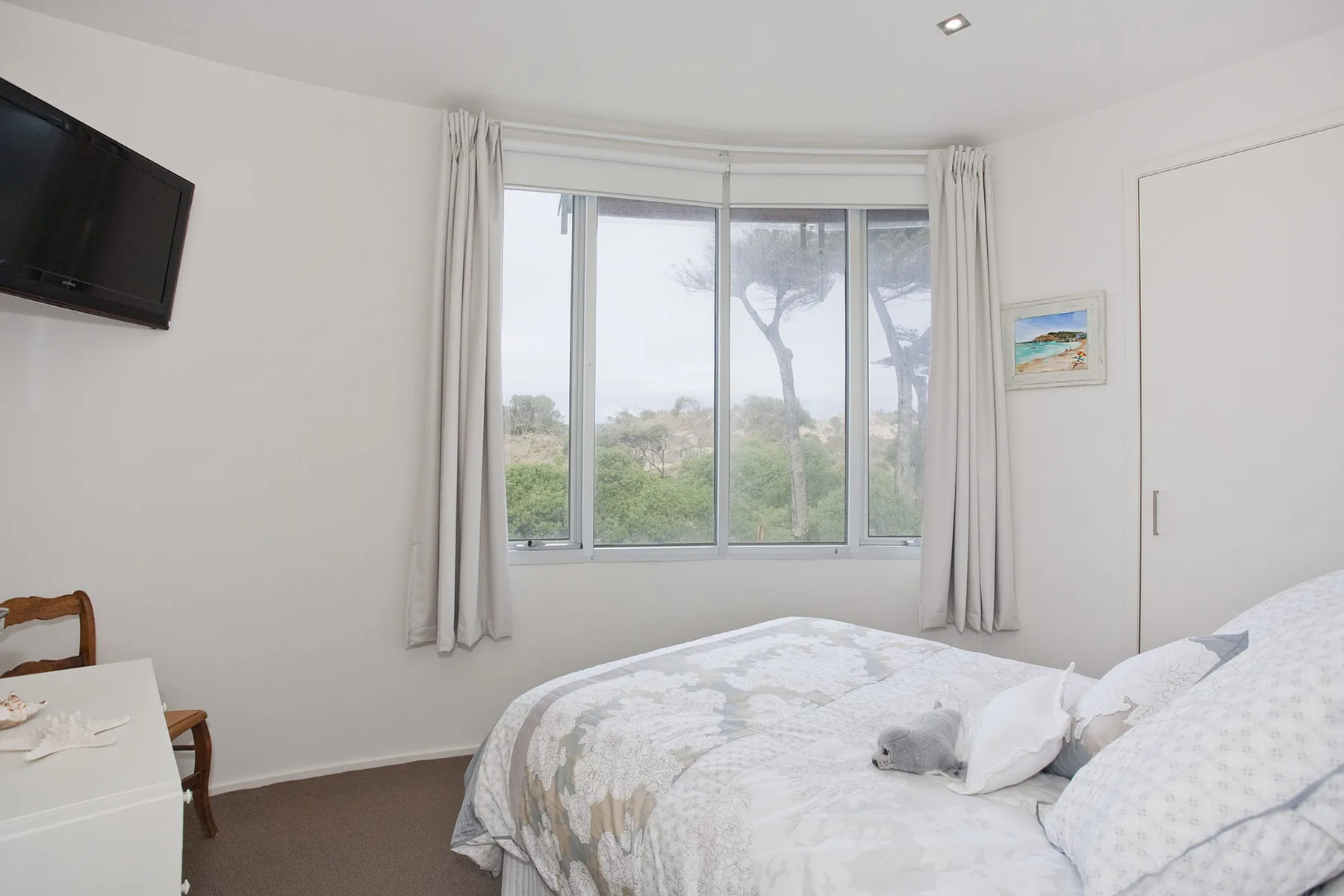 Un dormitorio luminoso con una cama grande junto a una ventana con vistas a zonas verdes.
