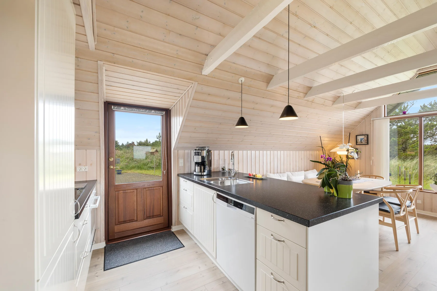 Una cocina luminosa con una encimera oscura y un comedor junto a grandes ventanas.