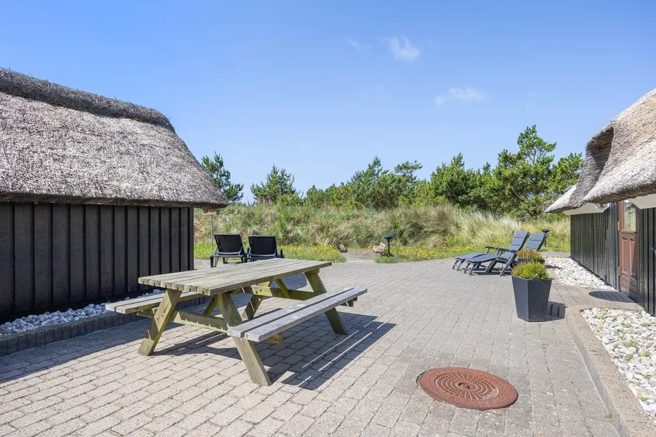 Un patio al aire libre con mesas de picnic, asientos y edificios con techo de paja.