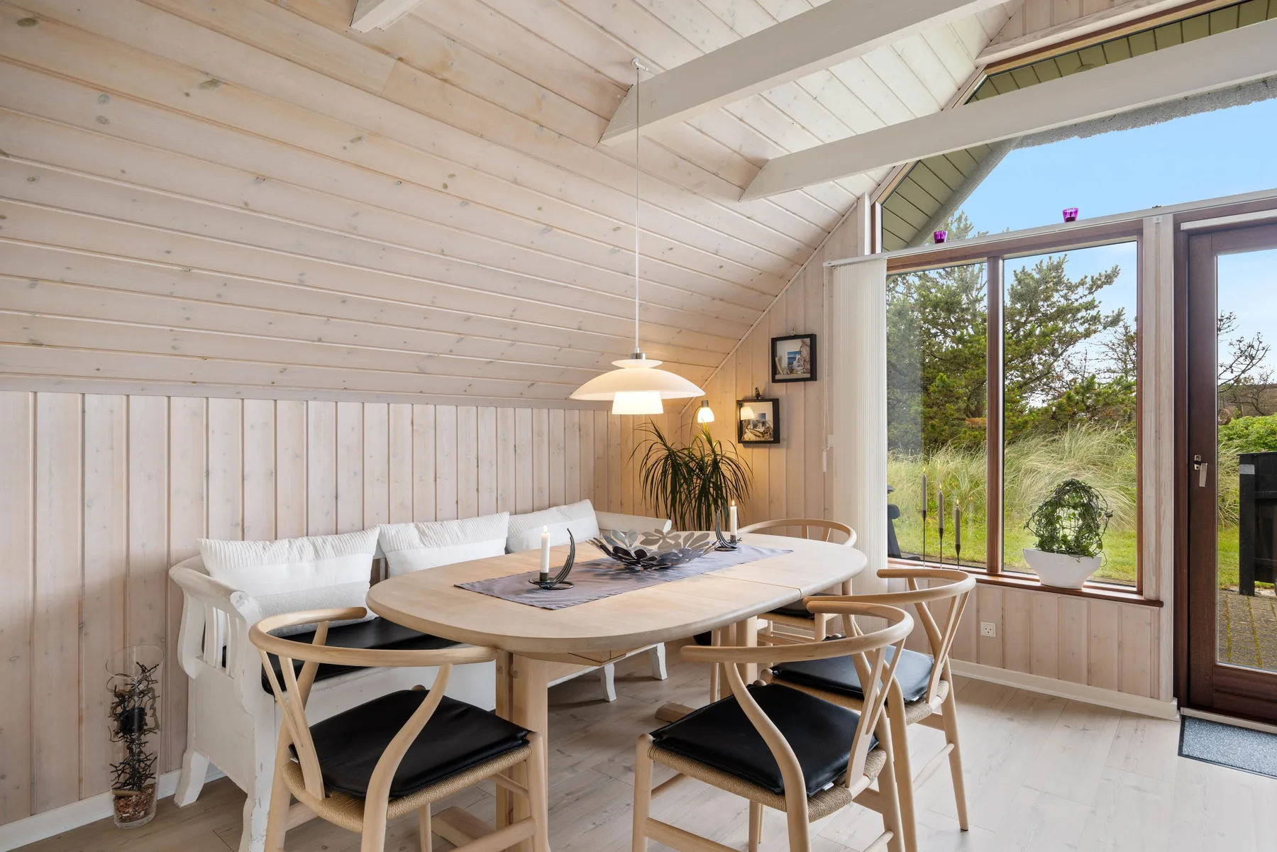 Comedor con mesa de madera y asientos junto a grandes ventanas.