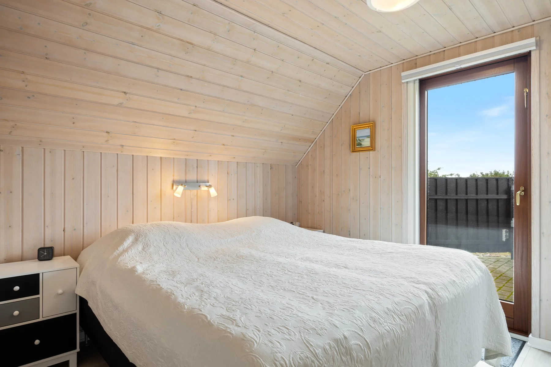 Dormitorio con una cama bajo un techo de madera inclinado y una puerta abierta.