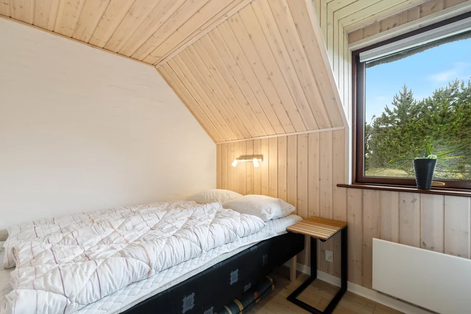 Un dormitorio con una cama bajo un techo inclinado revestido de madera.