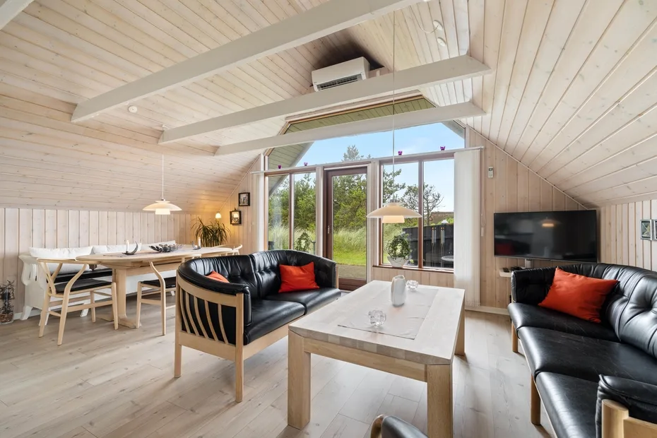 Una luminosa sala de estar y comedor tiene asientos negros y una mesa junto a grandes ventanas.