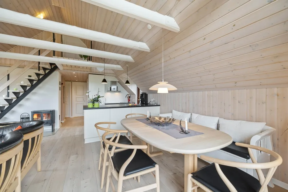 Comedor con una mesa larga y sillas bajo un techo inclinado revestido de madera.