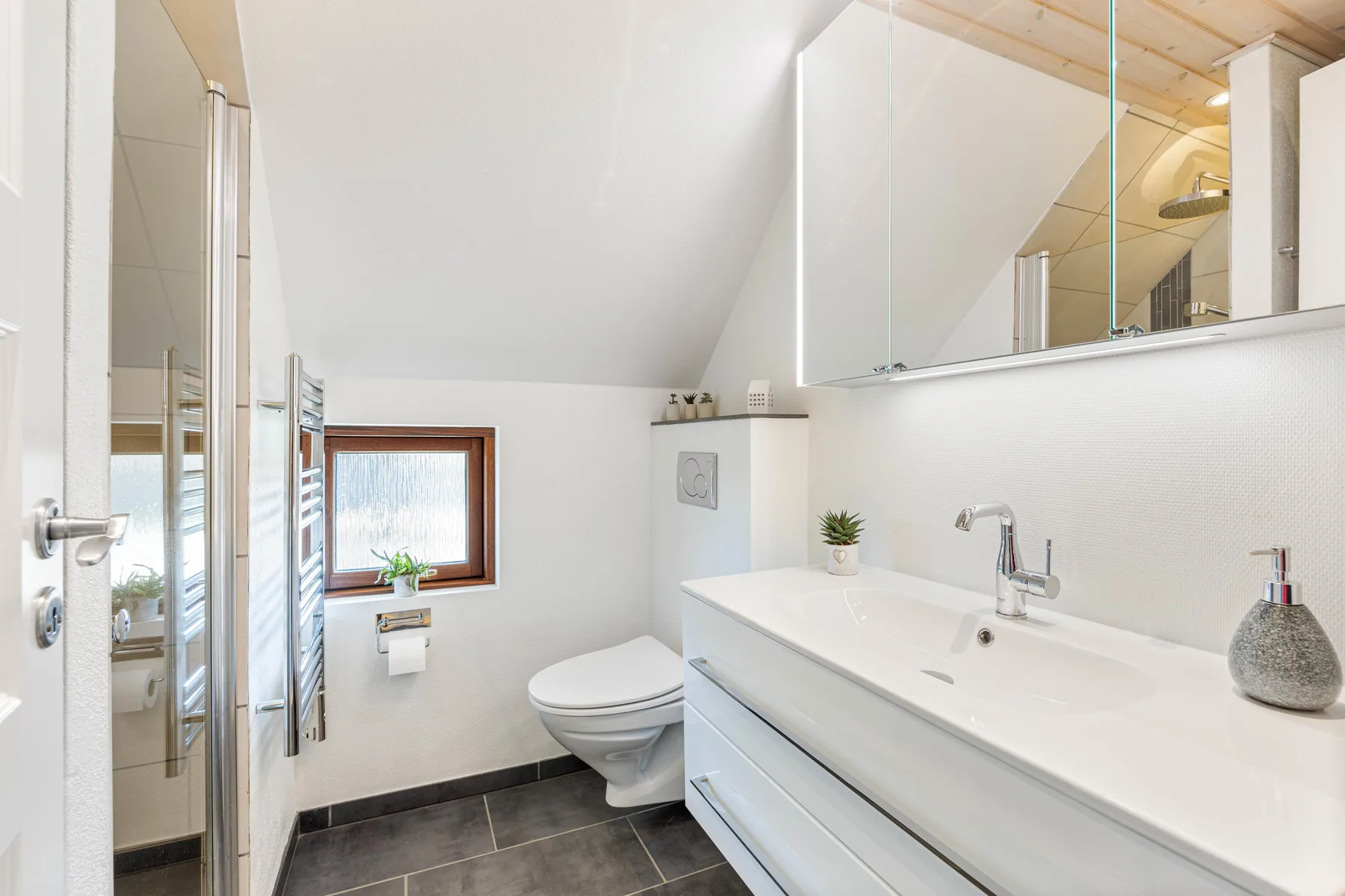 Un baño luminoso con ducha, inodoro y un largo lavabo.