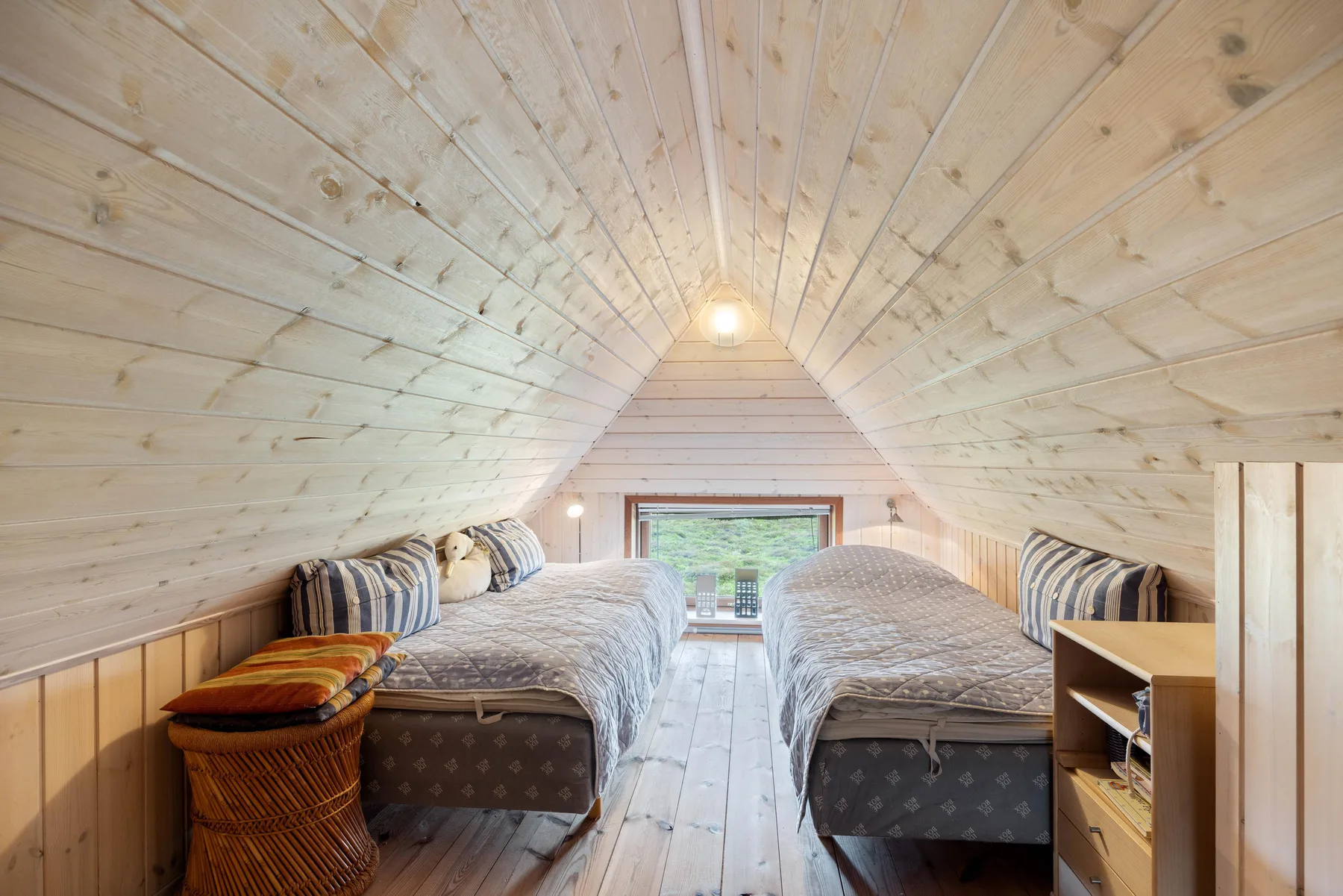 Un dormitorio abuhardillado luminoso con dos camas bajo un techo de madera inclinado.