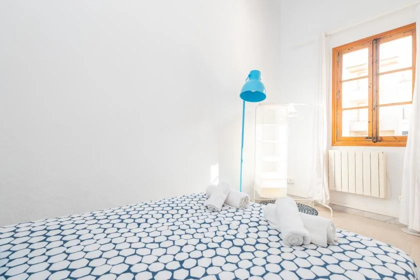 A bright bedroom with patterned bedding and a wooden-framed window.