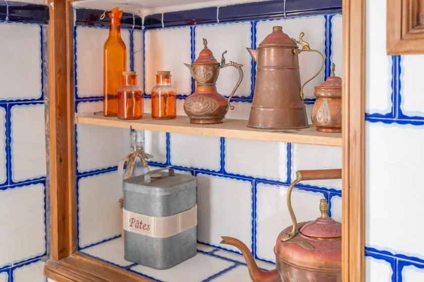 A tiled kitchen shelf displays metal coffee pots and glass bottles.