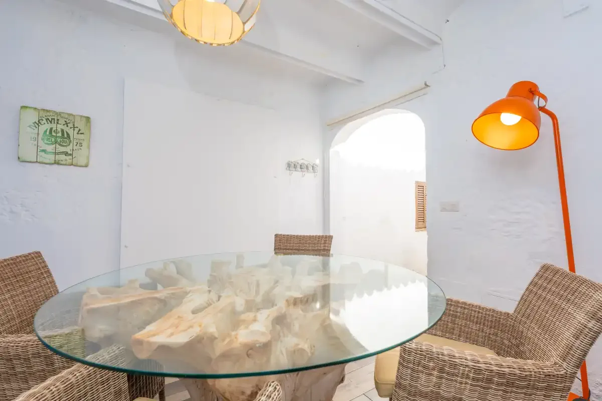 A bright dining area features a glass table and woven seating.