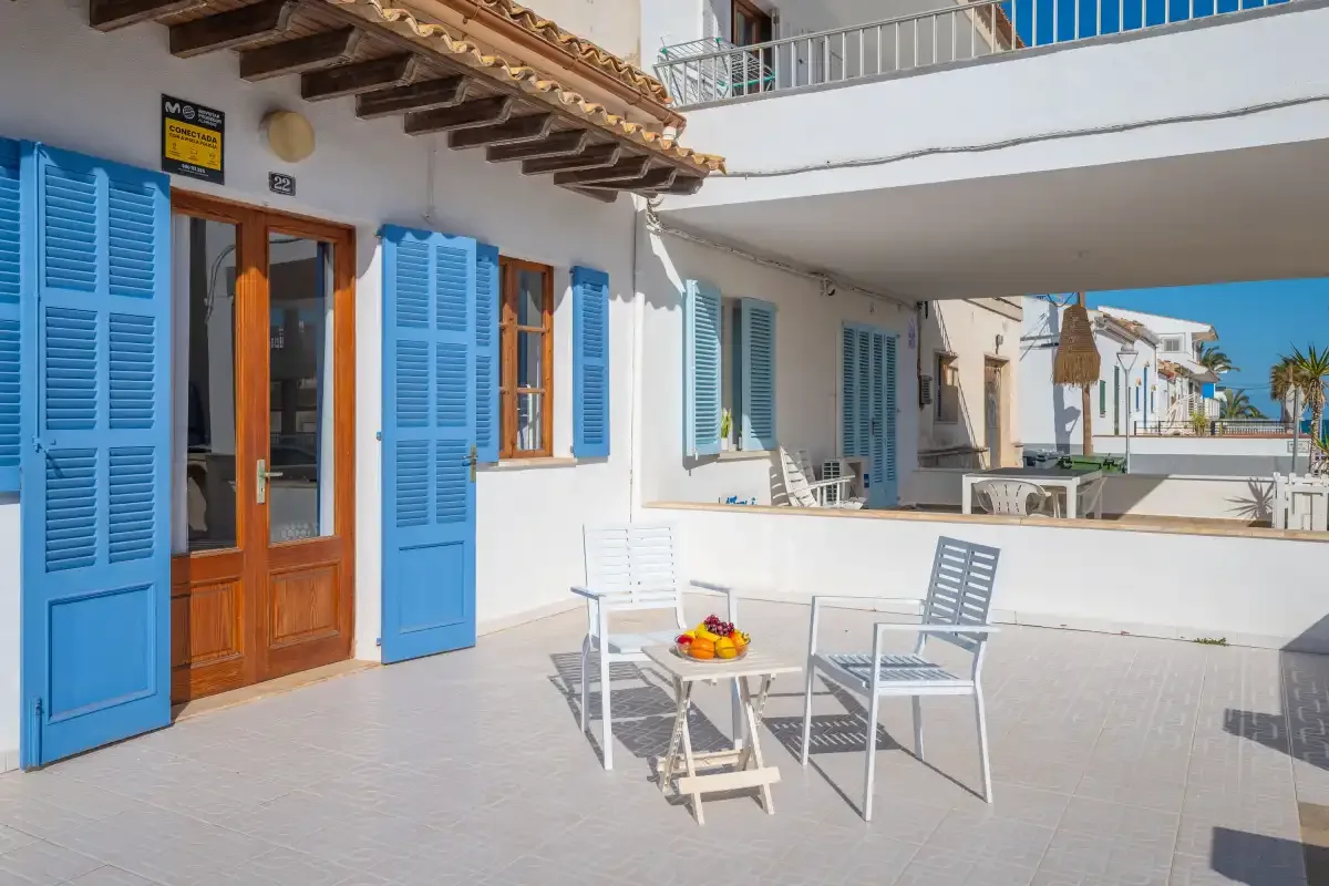 A sunny patio with outdoor seating beside a white building with blue shutters.