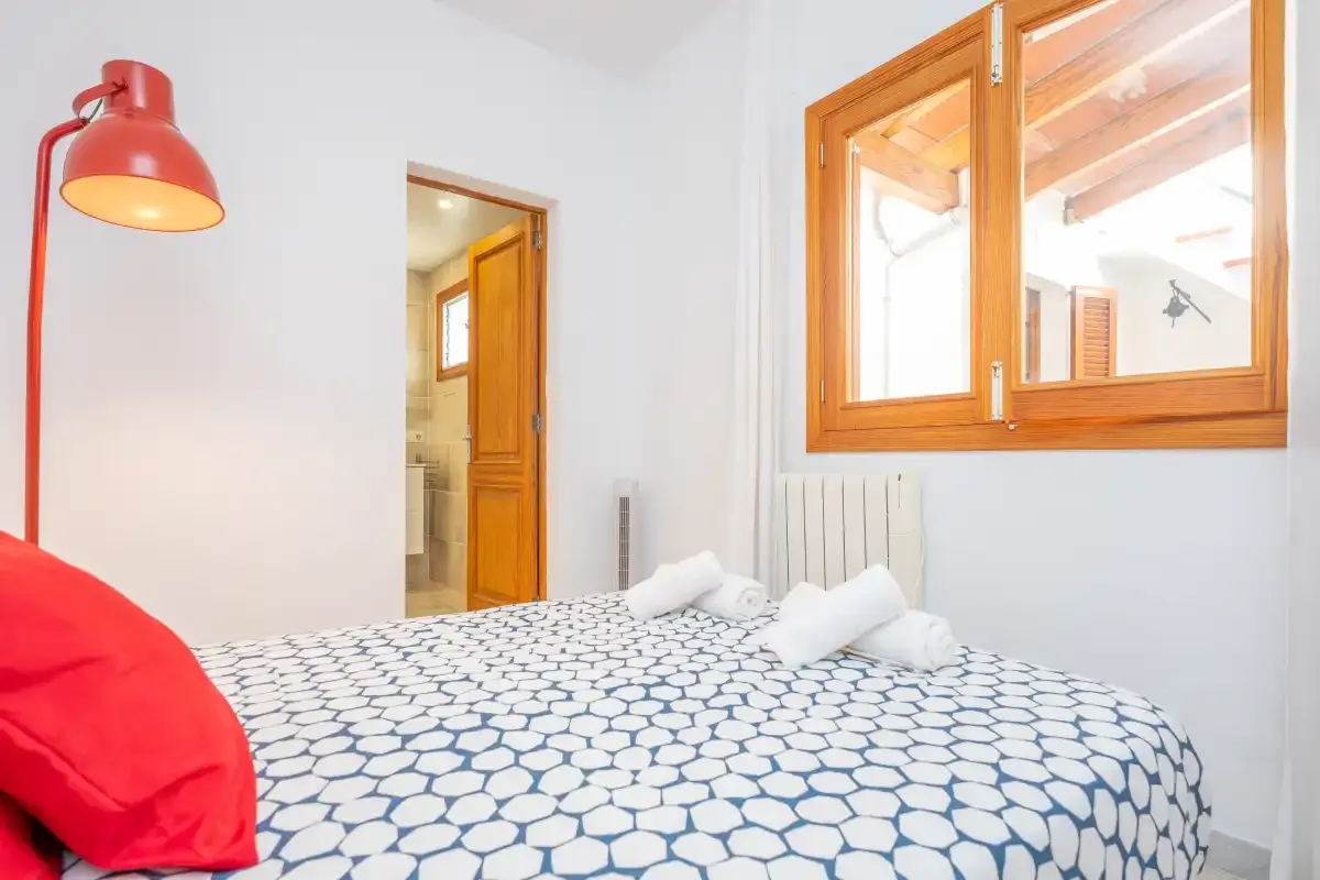A bedroom with patterned bedding and a red reading lamp beside the bed.