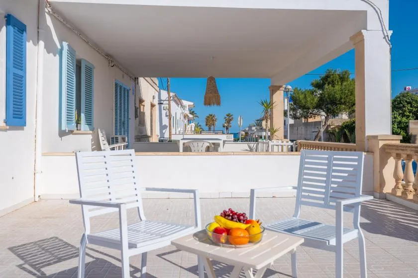 A covered outdoor terrace with white seating and a table of fruit.