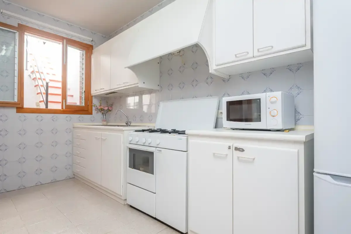 A bright kitchen with white cabinets, a stove, and a microwave.