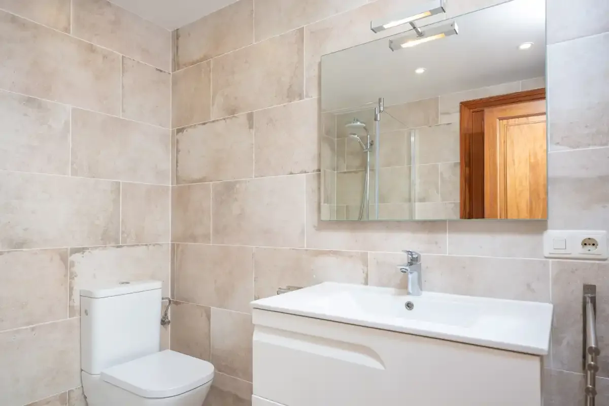 A tiled bathroom with a sink, toilet, and wall mirror.