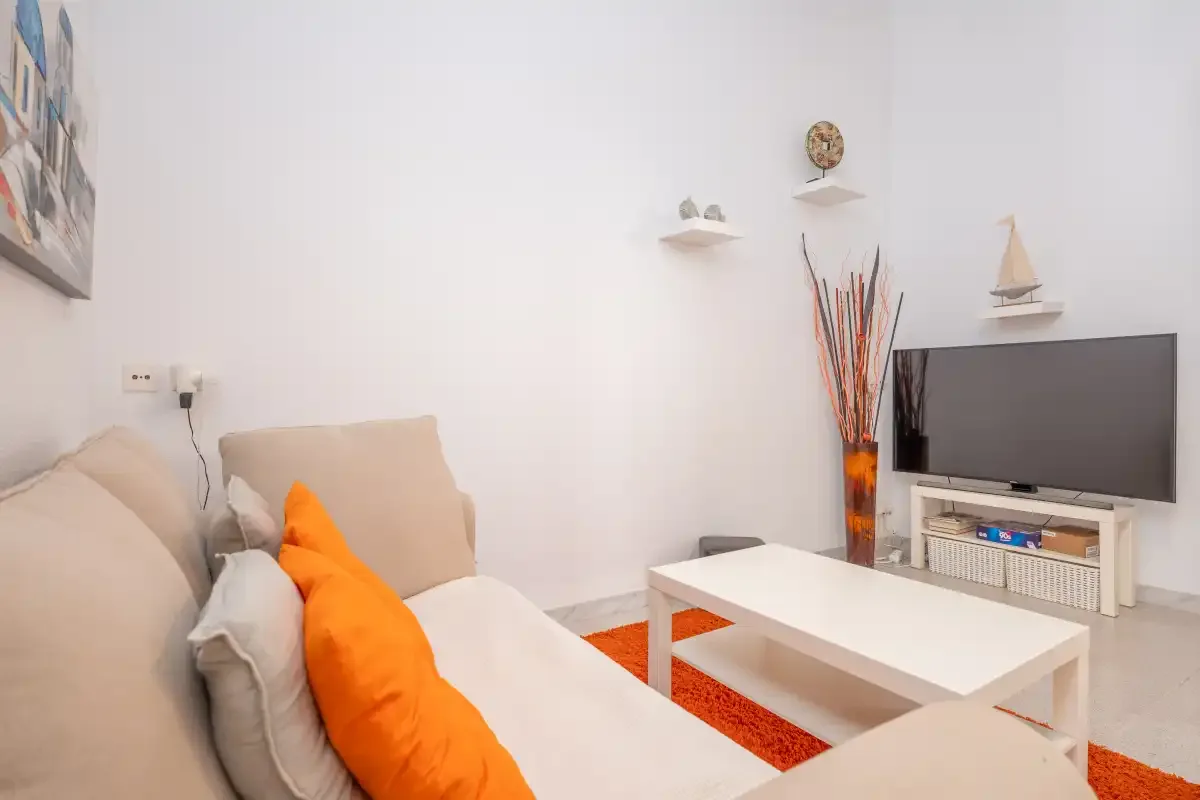 A living room with a light-colored sofa, white coffee table, and television.