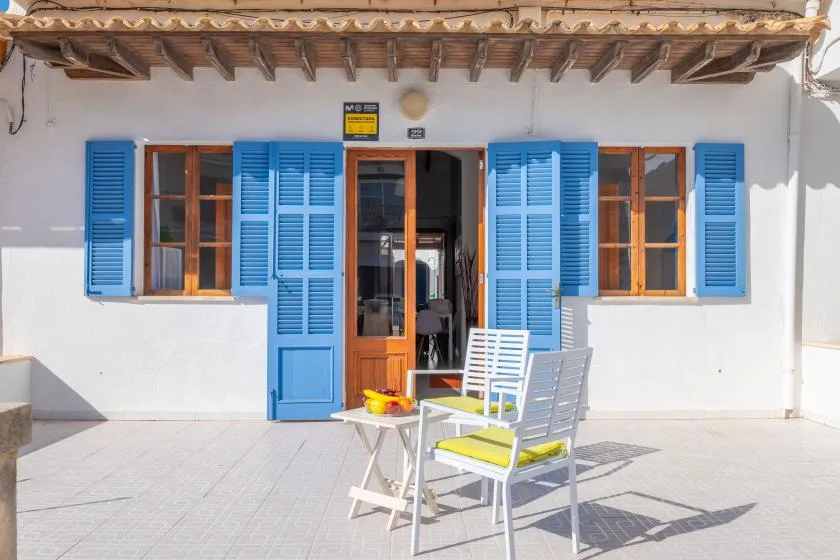 A sunny patio with white seating and bright blue shutters around the doorway.