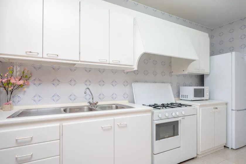 A bright kitchen with white cabinets, a sink, and a stove.
