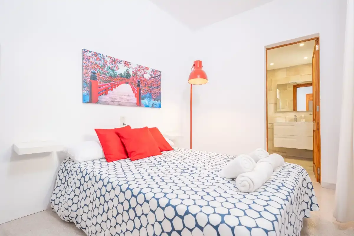 A bedroom with a patterned bedspread, red pillows, and a red floor lamp.