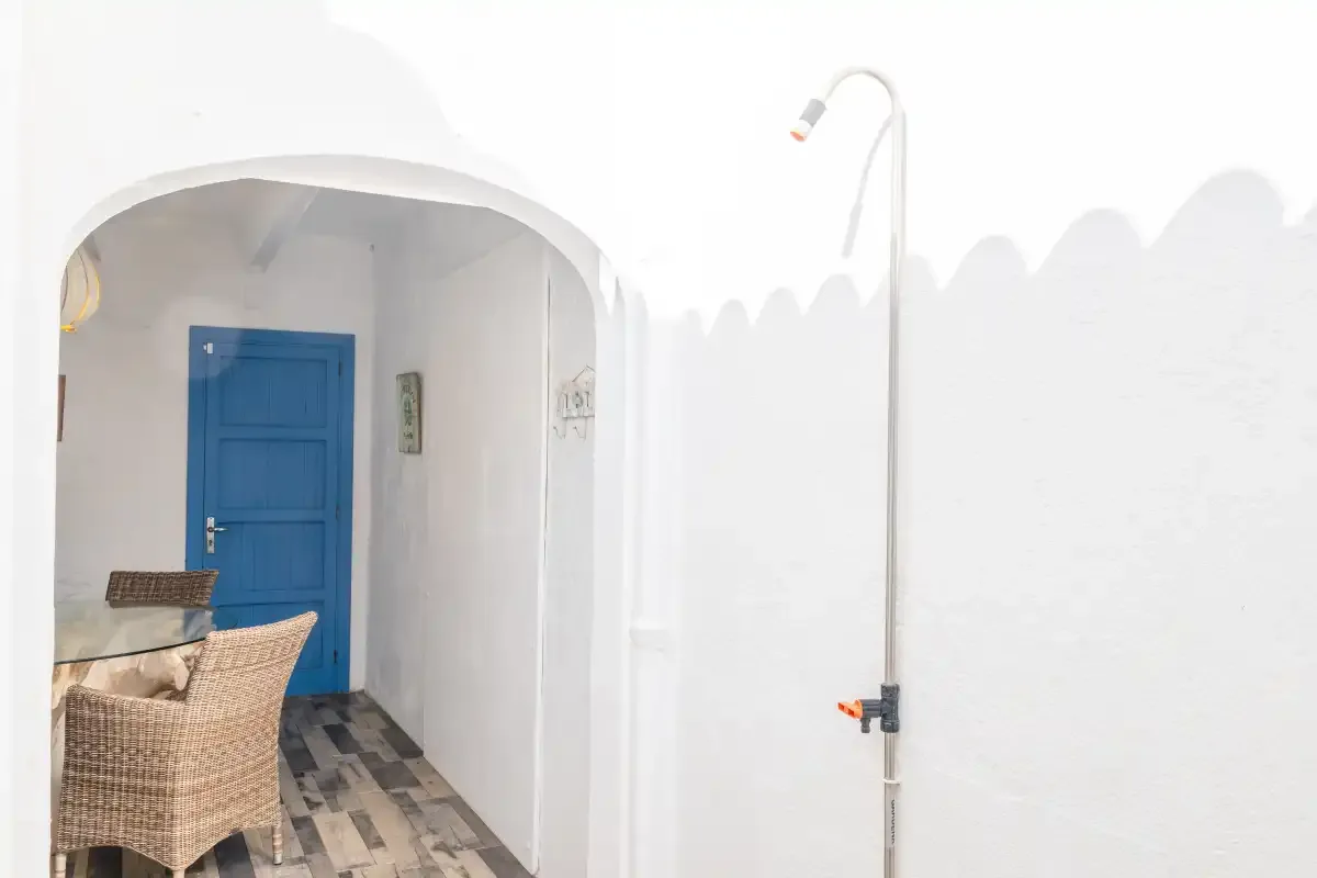 A white outdoor shower area with a blue door and woven seating.