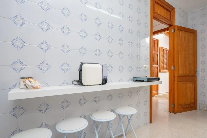 A tiled kitchen counter with a small appliance and stools beside an open wooden door.