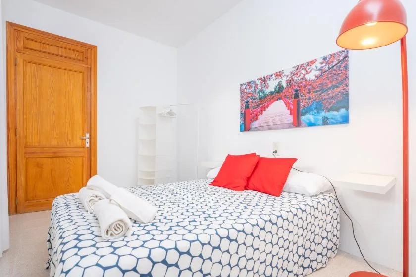 A bedroom with a patterned bedspread, red pillows, and a colorful wall print.