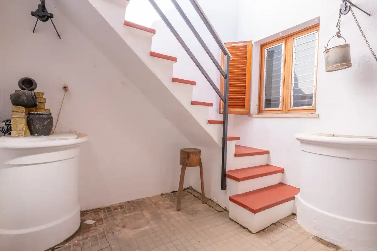 A tiled interior with a staircase and a shuttered window.