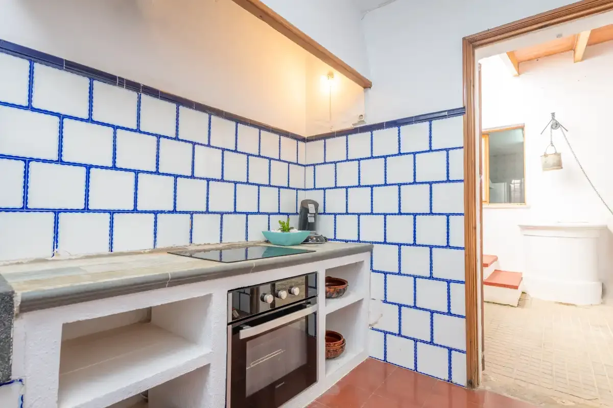A tiled kitchen with a countertop and built-in oven opens onto a bathroom.