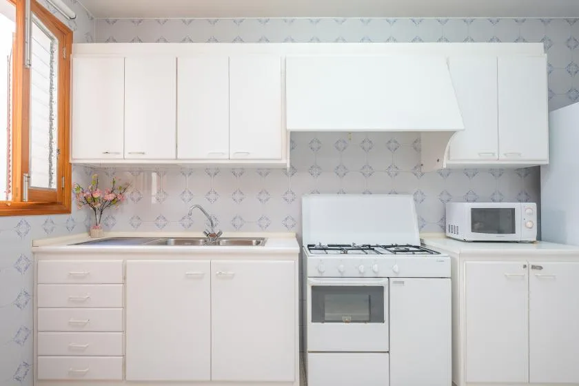 A bright kitchen with white cabinets, a sink, and a gas stove.