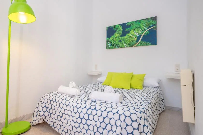 A bedroom with a bed covered in patterned bedding and bright green pillows.