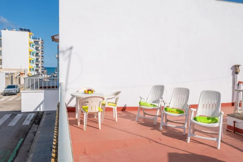 A sunny terrace has seating around a small table beside a white wall.