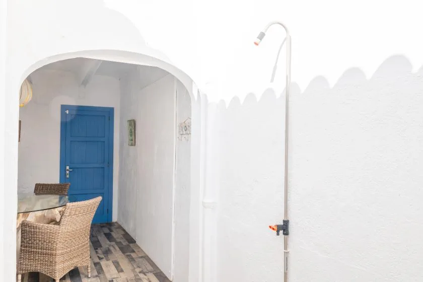 A white courtyard passage leads to a blue door, with woven seating nearby.