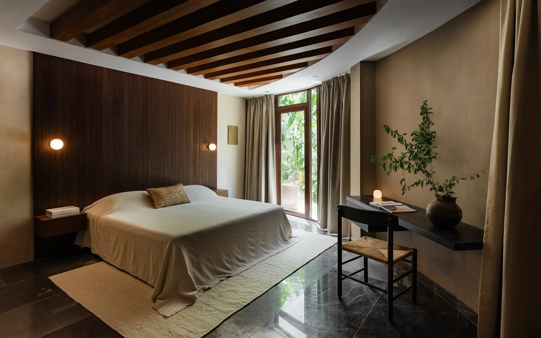 A bedroom with a bed, a desk, and glass doors opening to greenery.