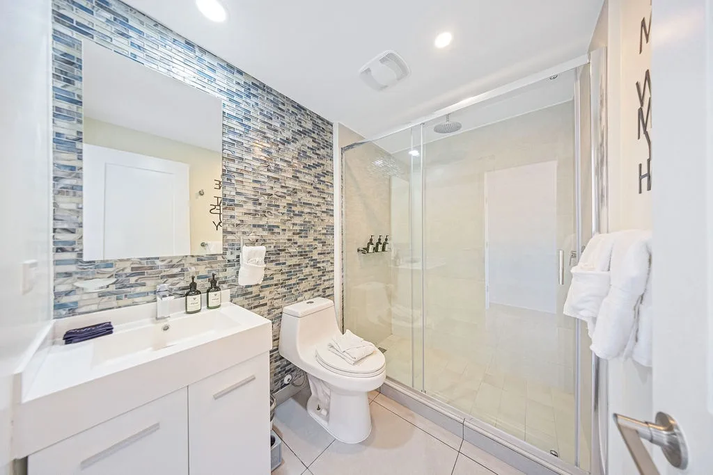 Step into your private spa-like retreat featuring a sleek glass shower, chic blue mosaic accent wall, and plush white towels waiting just for you.