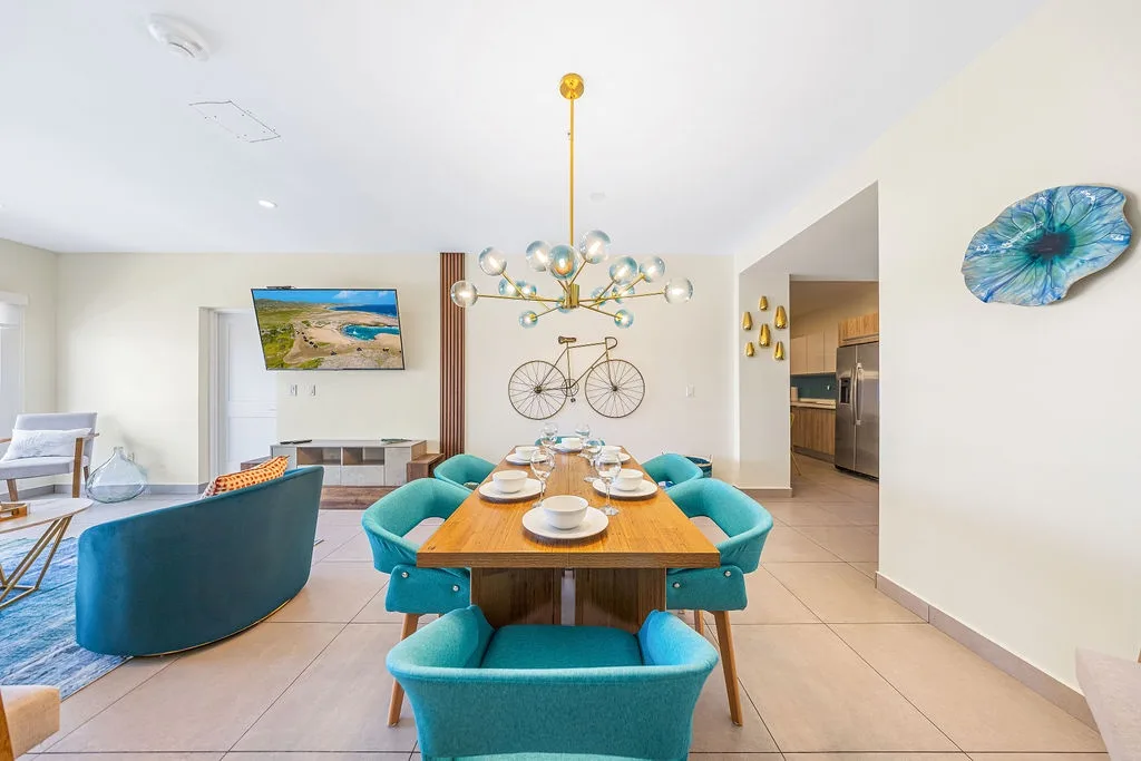 Gather around the elegantly styled dining table where modern coastal design meets comfort. The plush teal seating and artistic touches create an inviting space for your memorable meals together.