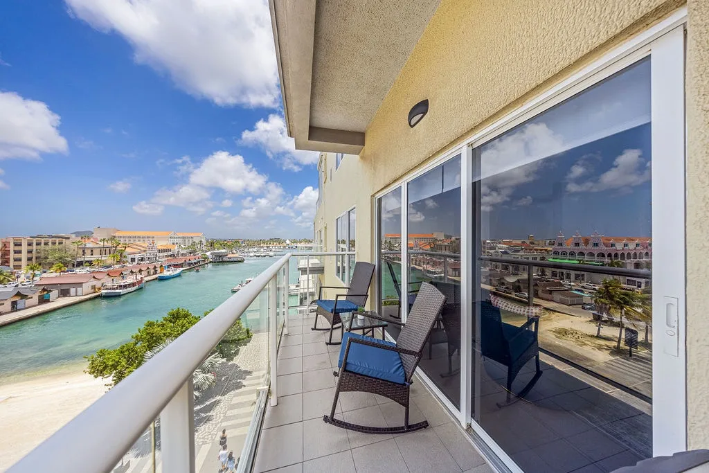 Imagine sipping your morning coffee here on this private balcony, gazing over turquoise waters and colorful buildings. Your perfect getaway awaits with two cozy lounge chairs and endless coastal views.