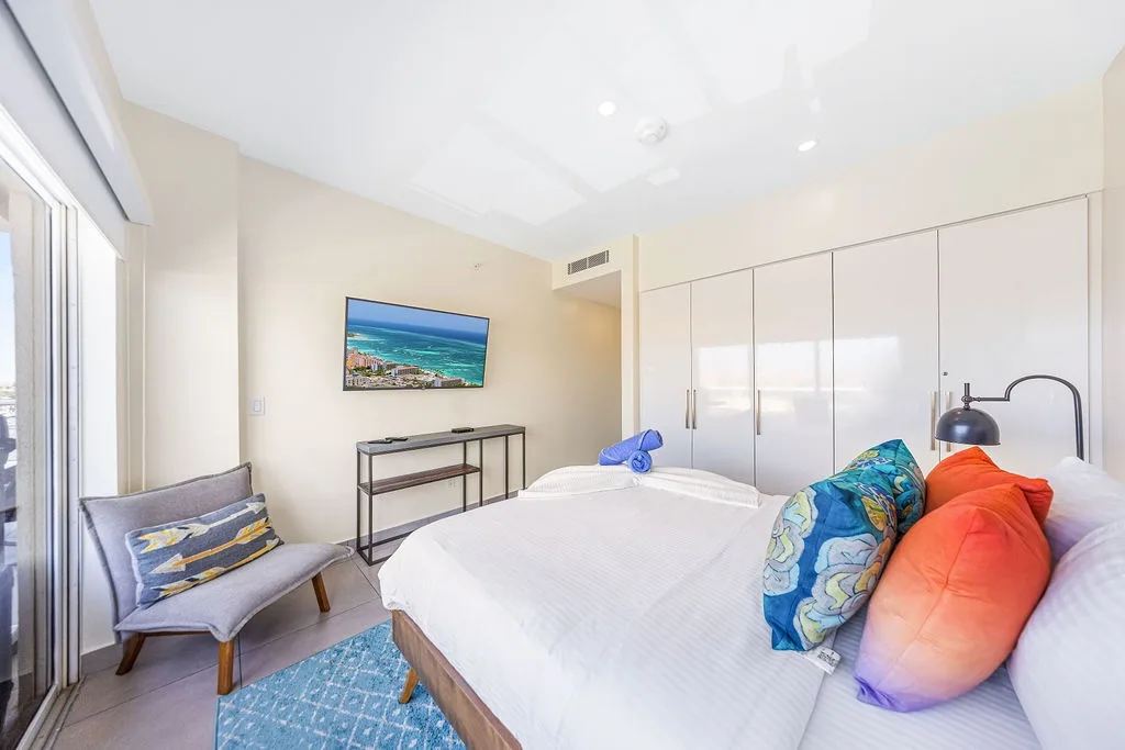 Your serene bedroom features a plush bed dressed in fresh linens and pops of color, sleek built-in storage, climate control, and calming coastal art to help you unwind after a day of adventure.