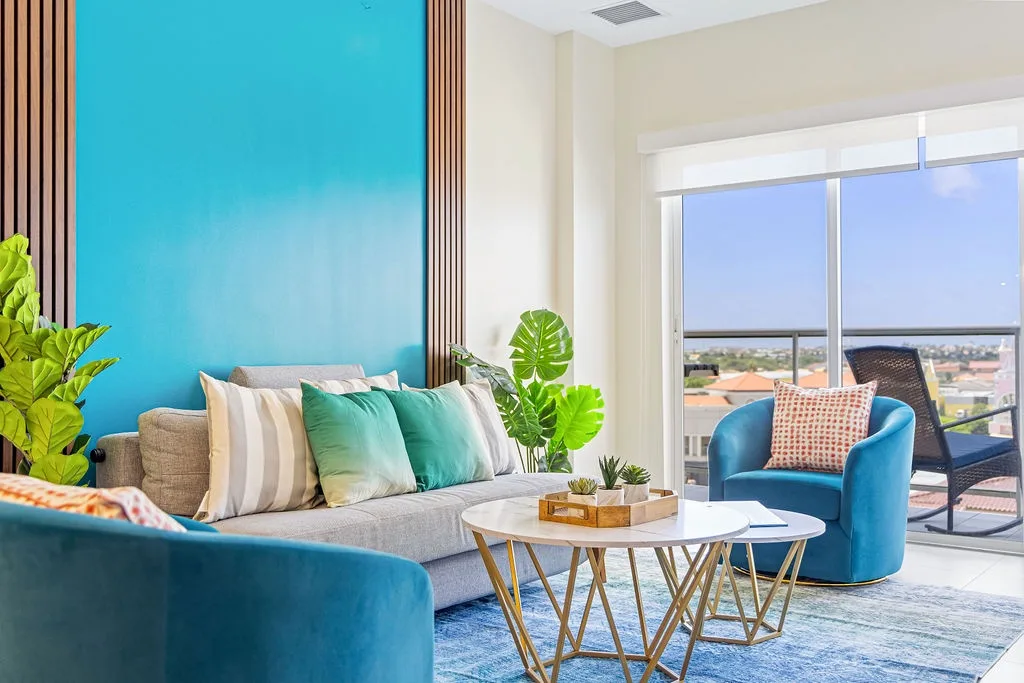 Relax in your bright living room with stylish turquoise and gray accents, lush greenery, and a private balcony overlooking the neighborhood.