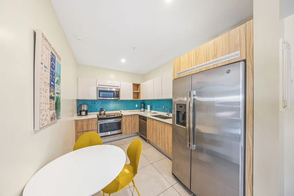 Your fully equipped kitchen features modern stainless-steel appliances, warm wood cabinetry, and vibrant turquoise tile backsplash. Cook comfortably at the sleek stove, store groceries in the spacious fridge, and enjoy meals at the cheerful dining table.