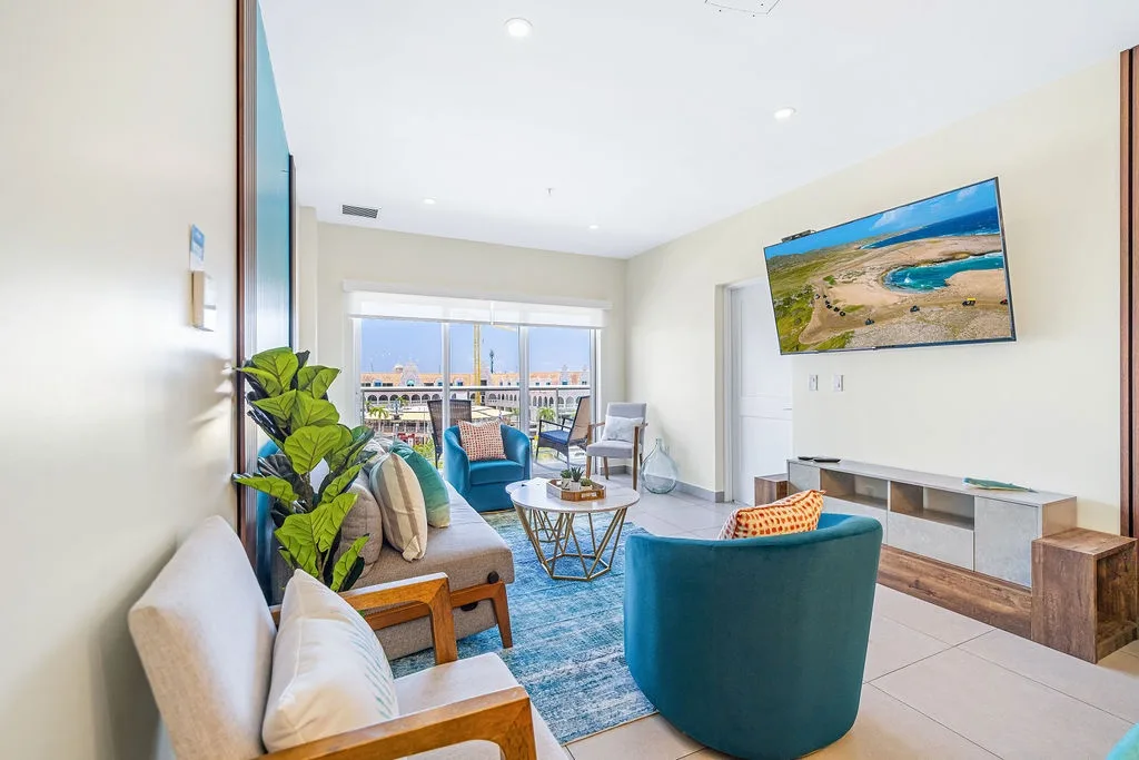 Settle into this bright living room where teal accents and natural light create a relaxing coastal vibe. Your favorite show awaits on the wall-mounted TV while balcony views beckon beyond.