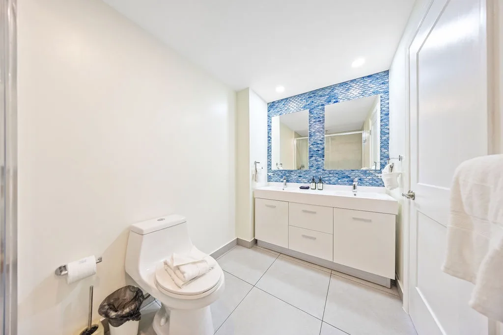 Bright, modern bathroom with a stunning blue mosaic accent wall and dual vanity mirrors. Fresh towels await your arrival, and the spacious layout makes getting ready a breeze.