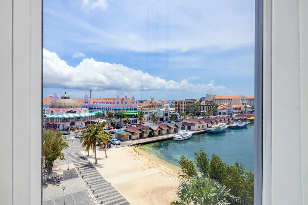 Elevated view showcasing the colorful waterfront district, sandy beach, and marina with boats, framed by tropical palms and Caribbean architecture beneath a bright sky with puffy clouds.