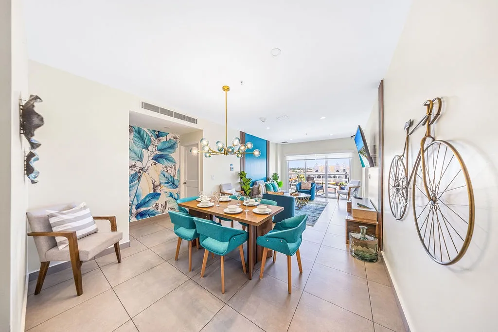 Step into your open-plan dining and living area, where vibrant turquoise accents and artistic touches create a welcoming, modern retreat for gathering and making memories.