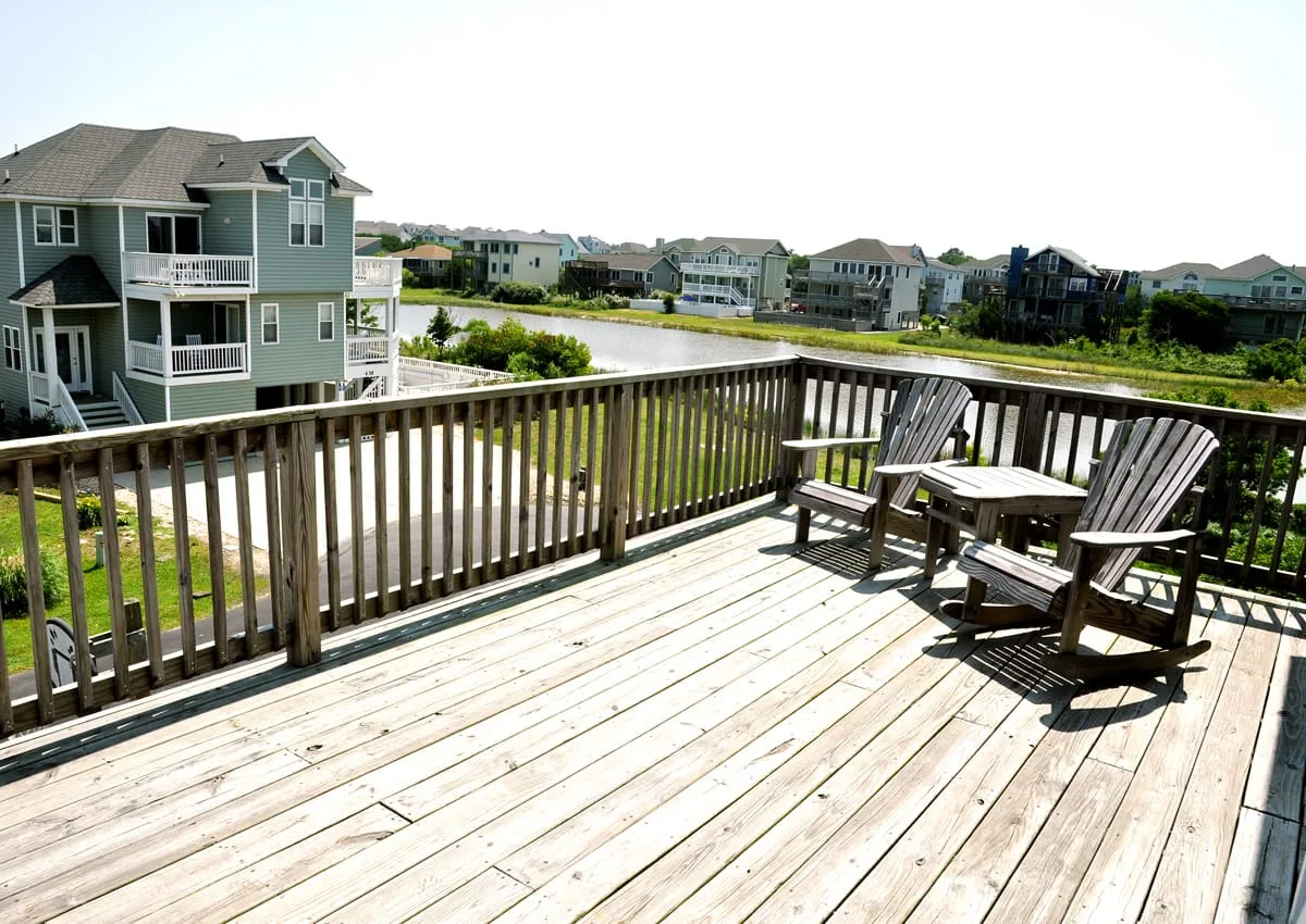 A wooden deck overlooks a pond, with outdoor seating beside the railing.