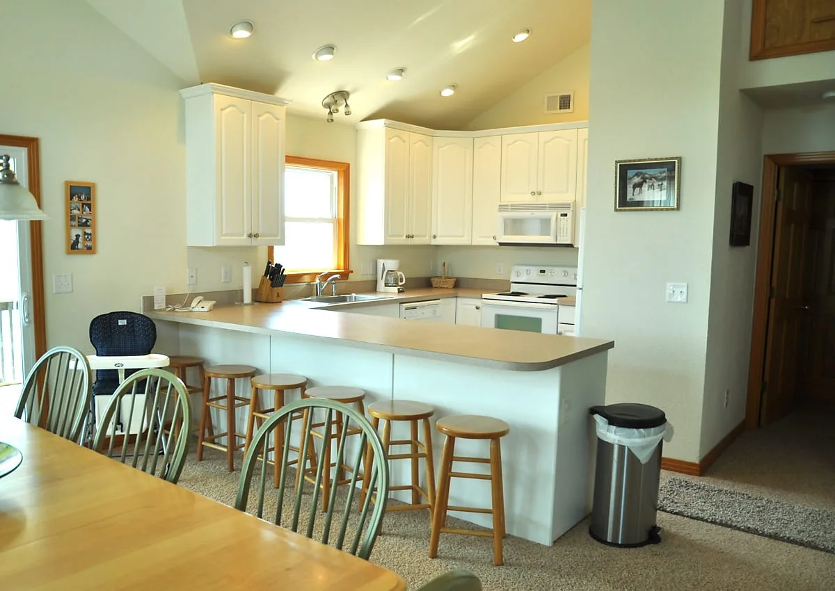 A bright kitchen with a counter, stools, and white cabinets.