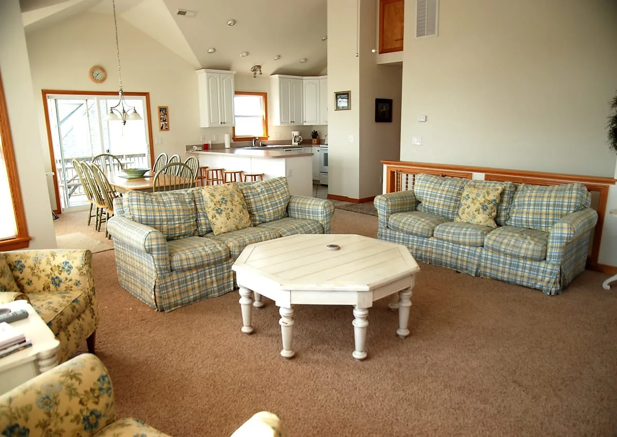 A living room with plaid seating and a white coffee table, with a dining area beyond.